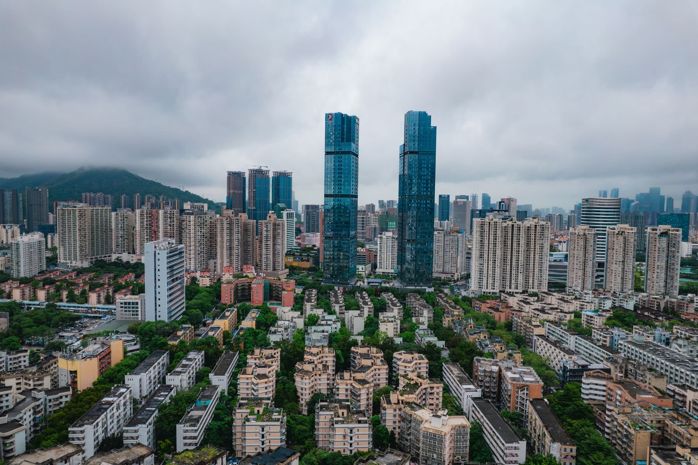 Aerial view of Nanshan, Shenzhen: low-rise housing blocks among trees, residential towers and twin glass skyscrapers